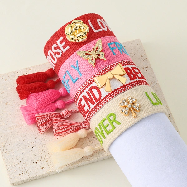 Tassel bracelets featuring embroidered words and decorative charms- rose, butterfly, clover, and bow